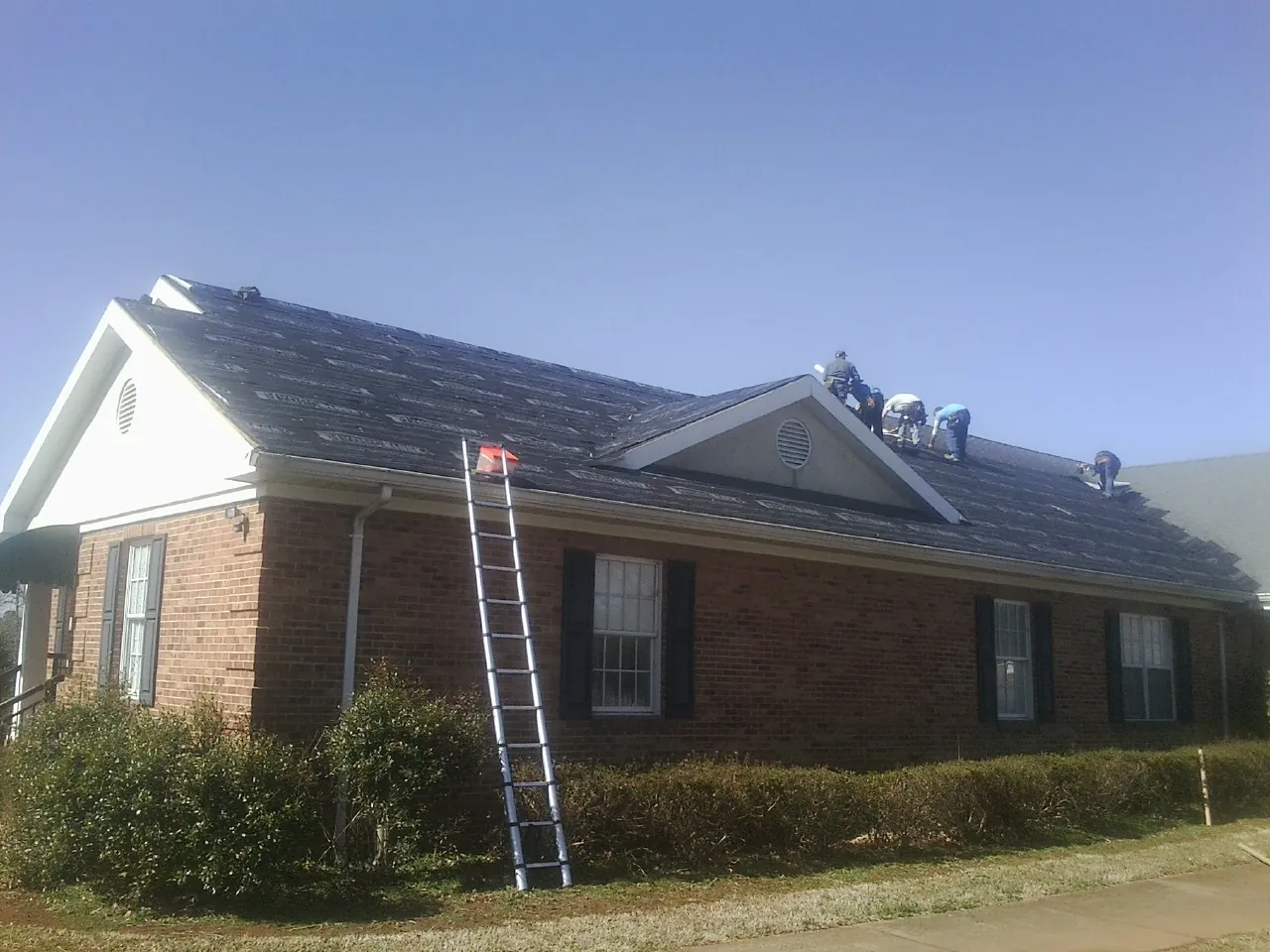 Crew tearing shingles off a brick ranch roof with a ladder set — Metal Roof Repair work by our crew in Mifflinburg