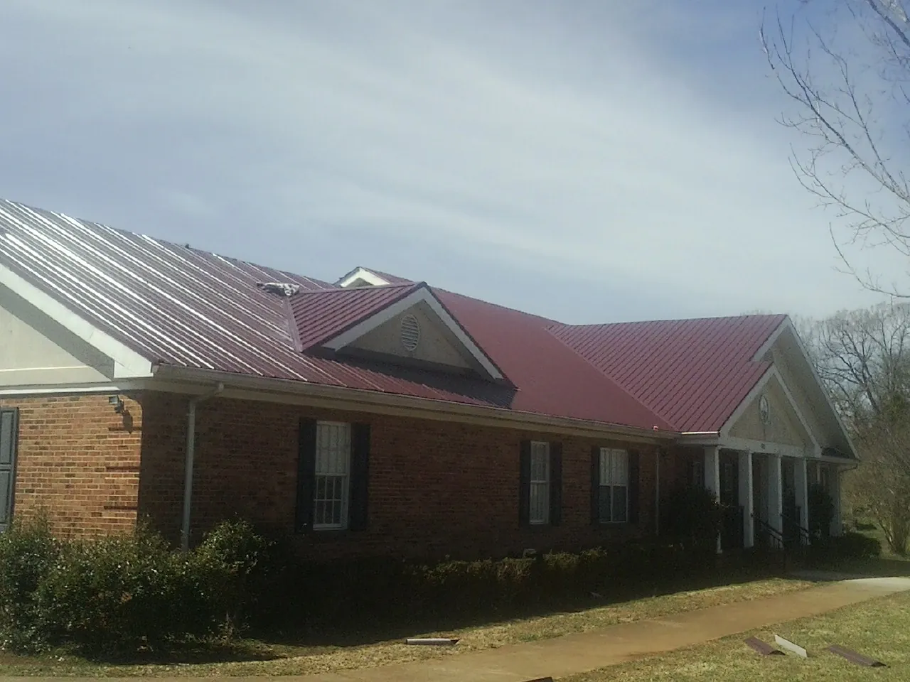 Red metal roof with gabled entries on a long brick building, from a Hail Damage Roof Repair job in Mifflinburg