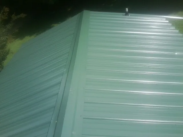 New green metal panels meeting at the ridge of a roof — Flat Roof Repair work by our crew in Mifflinburg