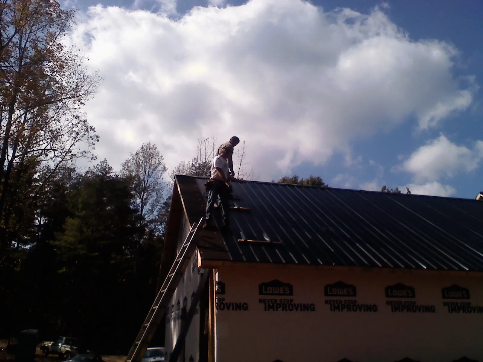 Roofer fastening dark metal panels high against a cloudy sky, from a Roof Inspection job in Mifflinburg