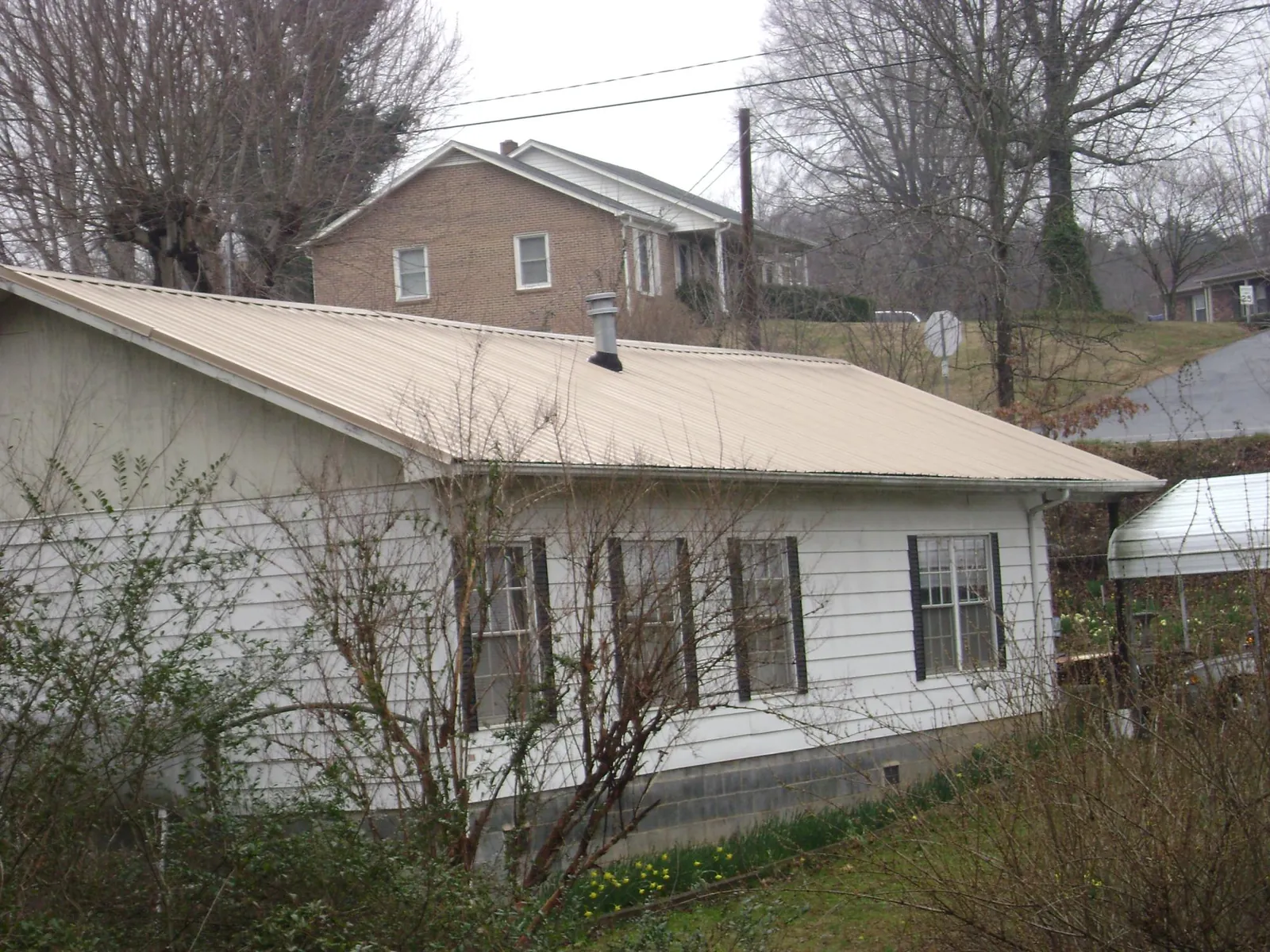 Tan metal roof on a white sided house set into a hillside — Commercial Roofing by Roofing Brothers in Mifflinburg